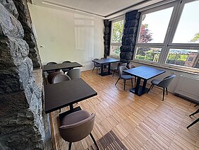 Heller Sitzbereich im sanierten Berggasthaus auf dem Pfaffenberg mit modernen Tischen, großen Fensterflächen und historischer Natursteinwand.