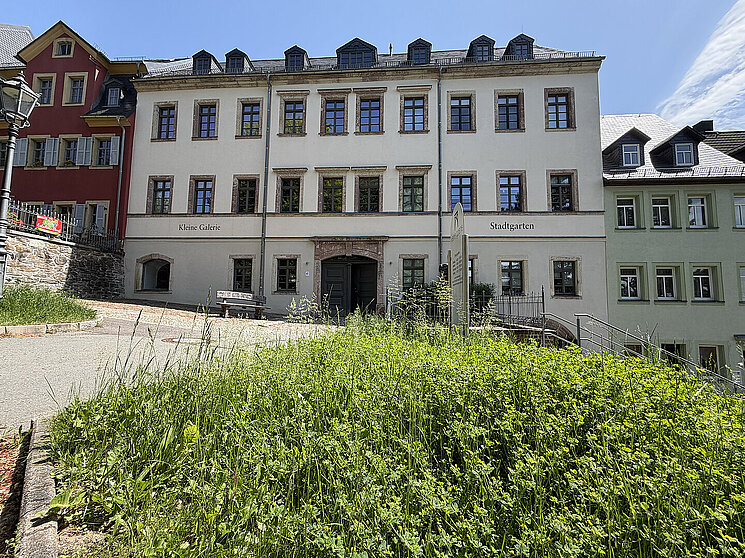 Außenansicht der Kleinen Galerie Hohenstein-Ernstthal im historischen Renaissance-Gebäude am Altmarkt mit heller Fassade, Stadtgarten und grünem Hangbereich im Vordergrund.