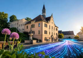Blick auf das Rathaus Hohenstein-Ernstthal an einem sonnigen Tag. Über den Marktplatz verlaufen symbolische leuchtende Glasfaser-Lichtlinien, die den digitalen Ausbau und die moderne Infrastruktur der Stadt darstellen.