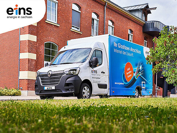 einsMobil von eins energie in sachsen steht auf einer Grünfläche vor einem roten Backsteingebäude und informiert vor Ort über den Glasfaserausbau in Hohenstein-Ernstthal.