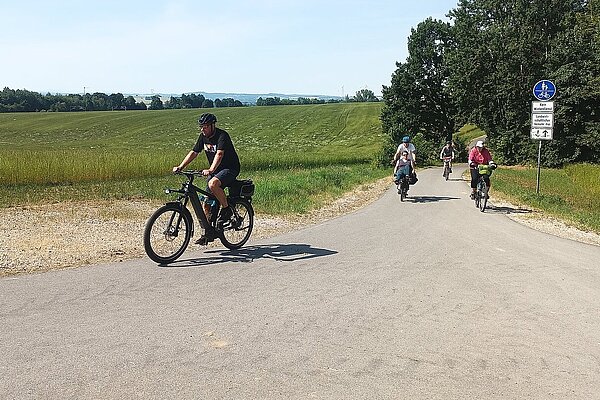 Mehrere Radfahrerinnen und Radfahrer fahren gemeinsam auf einem asphaltierten Radweg durch die offene Landschaft rund um Hohenstein-Ernstthal. Die Tour führt bei sonnigem Wetter über den Kohlebahnradweg und steht für gemeinsames Radfahren und Naturerlebnis in der Region.