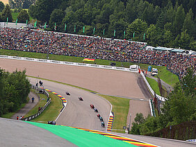 Motorrad Grand Prix Sachsenring 2025 Blick auf eine Kurve des Sachsenrings beim Motorrad Grand Prix Deutschland mit dicht besetzten Zuschauerhängen und mehreren Rennmaschinen im Pulk auf der Strecke – die große Fanmenge zeigt die besondere Atmosphäre der traditionsreichen Rennstrecke in Hohenstein-Ernstthal.
